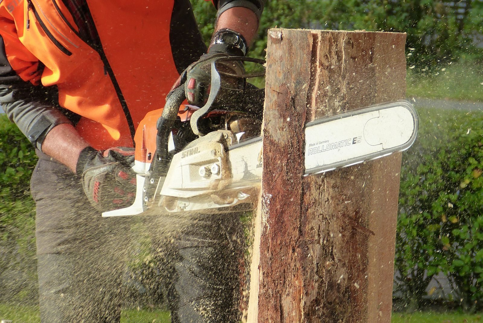 Tree surgeon in hi-vis cutting through a trunk with a chainsaw
